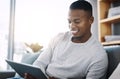 Alone time is always happy time. a handsome young man using his digital tablet while sitting on a sofa at home. Royalty Free Stock Photo