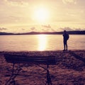 Alone traveler with backpack. Man on sea beach at wooden bench, cold sunny autumn evening Royalty Free Stock Photo