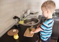 Alone vegetarian child cuts green cucumber with knife in kitchen, vegan kid helper, montessori training, side view Royalty Free Stock Photo