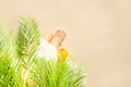 Alone woman sitting under palm tree branches with glass of water with piece orange. Female relaxation on the sand of the beach Royalty Free Stock Photo