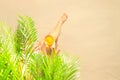 Alone woman sitting under palm tree branches with glass of water with piece orange. Female relaxation on the sand of the beach Royalty Free Stock Photo