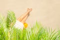 Alone woman sitting under palm tree branches with glass of water with piece orange. Female relaxation on the sand of the beach Royalty Free Stock Photo