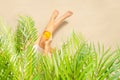 Alone woman sitting under palm tree branches with glass of water with piece orange. Female relaxation on the sand of the beach Royalty Free Stock Photo