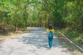 Alone woman traveller or backpacker walking along contryside road among green trees. Royalty Free Stock Photo