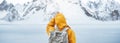 Alone woman wearing hipster backpack and yellow jacket standing in front of snowy mountains