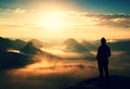 Alone young girl tourist feast autumn daybreak on the sharp corner of sandstone rock and watch over misty valley to Sun.