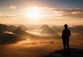 Alone young girl tourist feast autumn daybreak on the sharp corner of sandstone rock and watch over misty valley to Sun. Royalty Free Stock Photo