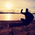 Alone Young Man In Silhouette Sitting In The Sun On Beach. Tourist take rest on wooden bench at autumn lake. Royalty Free Stock Photo