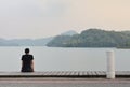 Alone young man sitting on wooden walkway looking to the mountain in the lake with sunset background