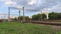 Along the fence and trees among the grassy lawns are electrified railroad tracks. The wires are attached to metal structures and c