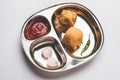 Indian food snack Aloo Bonda or potato pakoda or pakora served in a stainless steel plate with tomato ketchup