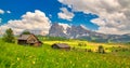 Alpe di Siusi - Seiser Alm with Sassolungo - Langkofel mountain group in background at sunset. Yellow spring flowers and wooden ch