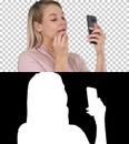 Beautiful young blonde woman which is painting her lips with red lipstick and looking in the phone, Alpha Channel Royalty Free Stock Photo