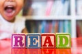 Alphabet blocks spelling the word read in front of a bookshelf and an excited child in the background Royalty Free Stock Photo