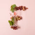 Alphabet. Letter F made of wineglasses with rose and white wine, grapes, leaves and corks lying on pink background. Wine Royalty Free Stock Photo