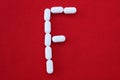 Alphabet made of pills on a red background. Abc from drugs.  Letter F made from pills. Capital letter F of medicines Royalty Free Stock Photo