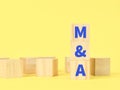 Alphabets M and A mergers and acquisitions on wooden cubes against yellow background.