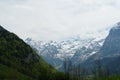 Alpine landscape In the springtime with hills covered by coniferous woods and mountains covered with snow on the background. Royalty Free Stock Photo