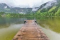 Tranquil spring summer foggy lake. Evergreen pine forest and mountain line under clouds and fog Royalty Free Stock Photo