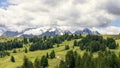 Alpine plateau with pine forests in the rays of the sun and the Dolomites covered with snow