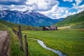 Alpine scene with dirt road rustic barn and snow runoff stream running through valley with wildflowers - snow peaked mountains Royalty Free Stock Photo