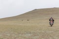 Altai, Mongolia. Mongolian men with his son ride motorbike at steppe. Boy looks at tourists