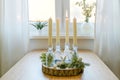 Alternative advent wreath, candles in bottles on a wooden board with decoration on a table at the window, one is lit, first sunday