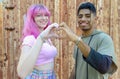 Alternative diverse couple hanging out together smiling and standing against a rusted background wall and holding hands in heart Royalty Free Stock Photo