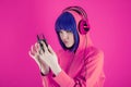 Portrait funky beautiful young woman with blue hair in hoodie on bright pink background. Alternative girl with headphone