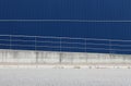 An aluminum blue cladding wall with an oblique railing in front of a sidewalk and an asphalt street.