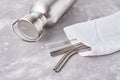 Aluminum bottle and metal tubes in cotton bag on a gray background. Reusable eco friendly items. Zero waste eco friendly concept