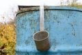 aluminum bucket hangs on a metal blue barrel in the autumn garden