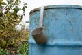 aluminum bucket hangs on a metal blue barrel in the autumn garden