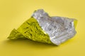 shiny aluminum foil wrap without chocolate candy on a yellow background. Texture of used crumpled aluminium food foil. Royalty Free Stock Photo