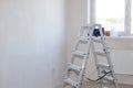 Aluminum folding staircase in a room with white plastered wall and window. Housing renovation in a new house. Copy space