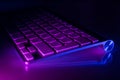 Aluminum keyboard illuminated in blue and purple mirroring on glass