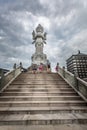 Low angle view of a family at Dragon Gate on stone steps next to a large Chinese statue with dramatic sky.