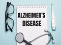 ALZHEIMERS DISEASE written on a white notepad next to a stethoscope, goggles, and an electronic thermometer on a light blue Royalty Free Stock Photo