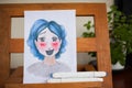 Amateur picture of girl with blue hair in anime style on wooden easel at home studio. Learning to draw emotions. A happy