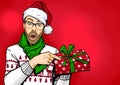 Amazed bearded man in glasses and Santa hat with open mouth showing gift box. Emotions and advertisement. Surprised men.