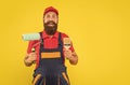 amazed bearded man housepainter in work clothes hold paint roller and brush on yellow background