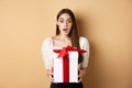 Amazed beautiful girl receiving gift from secret admirer on Valentines day, looking surprised at camera, holding box and Royalty Free Stock Photo