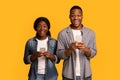Amazed black man and woman using smartphones over yellow studio background Royalty Free Stock Photo