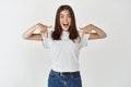 Amazed brunette girl pointing fingers down at your logo, standing excited at white background Royalty Free Stock Photo