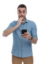 Amazed casual man holding phone, gasping and covering mouth