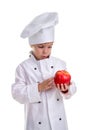 Amazed chef girl in a cap cook uniform, holding and examining the red apple. Human emotions, facial expression feeling