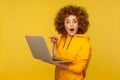 Amazed emotional bright woman with curly hair in urban style hoody pointing laptop screen and looking at camera Royalty Free Stock Photo