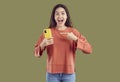 Amazed young brunette woman in casual clothes is pointing at smartphone on khaki background. Royalty Free Stock Photo