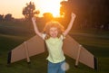 Amazed excited kid playing with toy plane on sunny golden sunset sky background outside on grassy summer hill. Dreaming