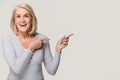 Amazed excited mature woman pointing at copyspace isolated on background